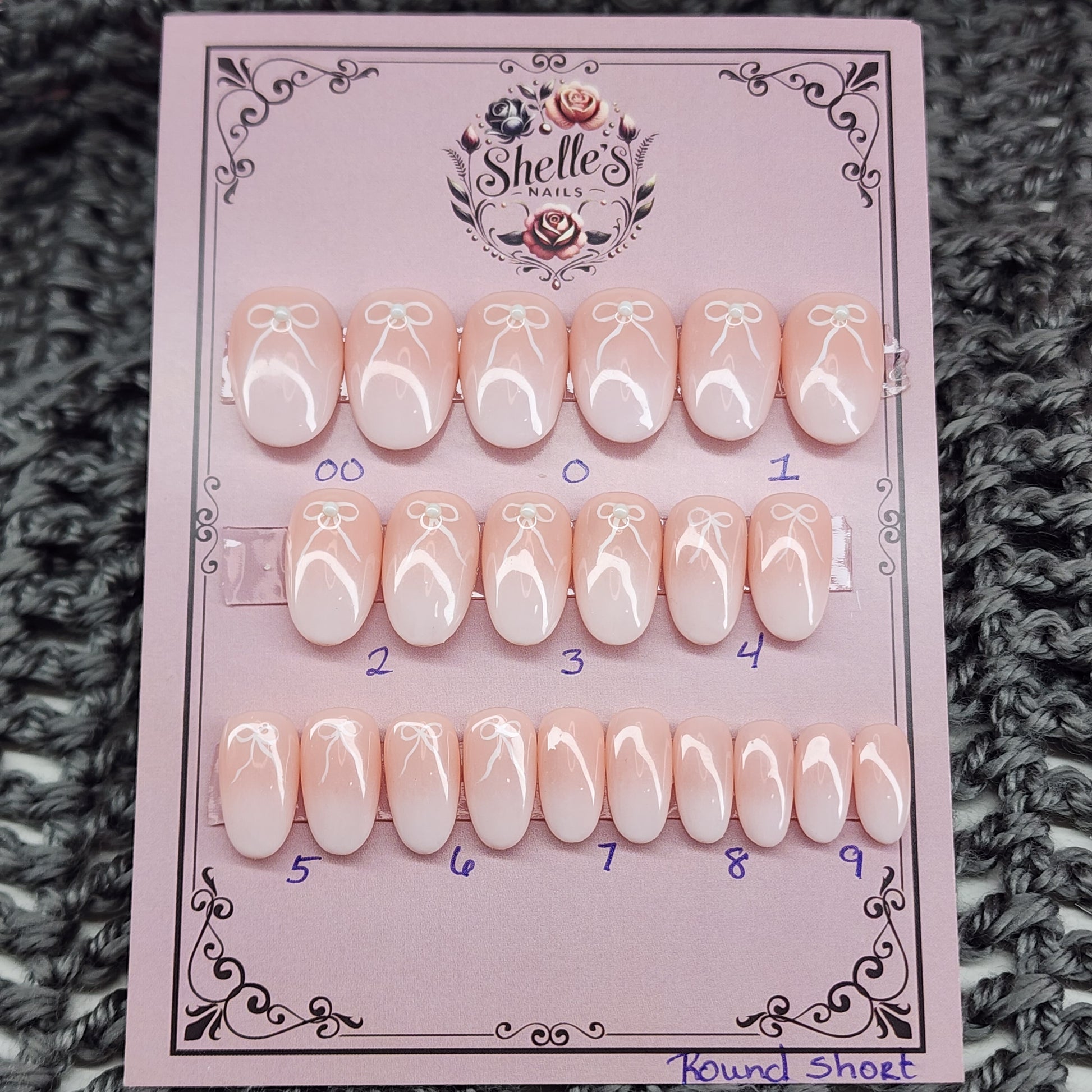 Peach nails with a white airbrush tip, bow and pearl accents in short round