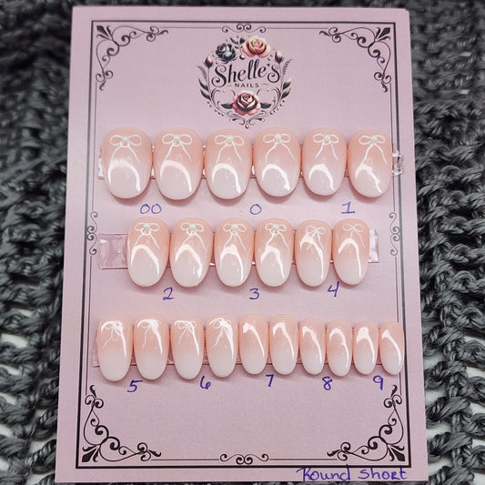 Peach nails with a white airbrush tip, bow and pearl accents in short round