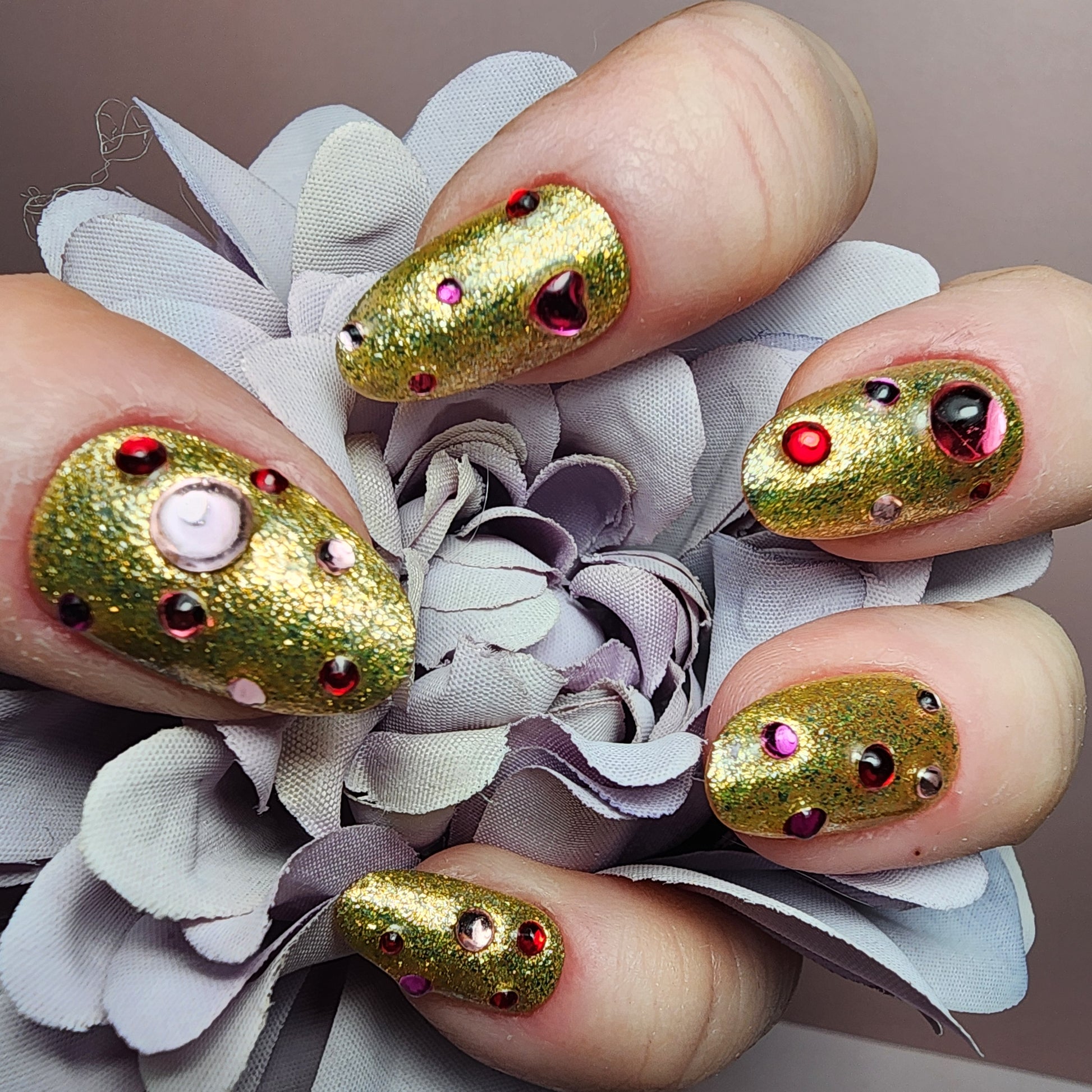 Gold glitter press-on nails featuring pink and red crystal gems with heart accents.