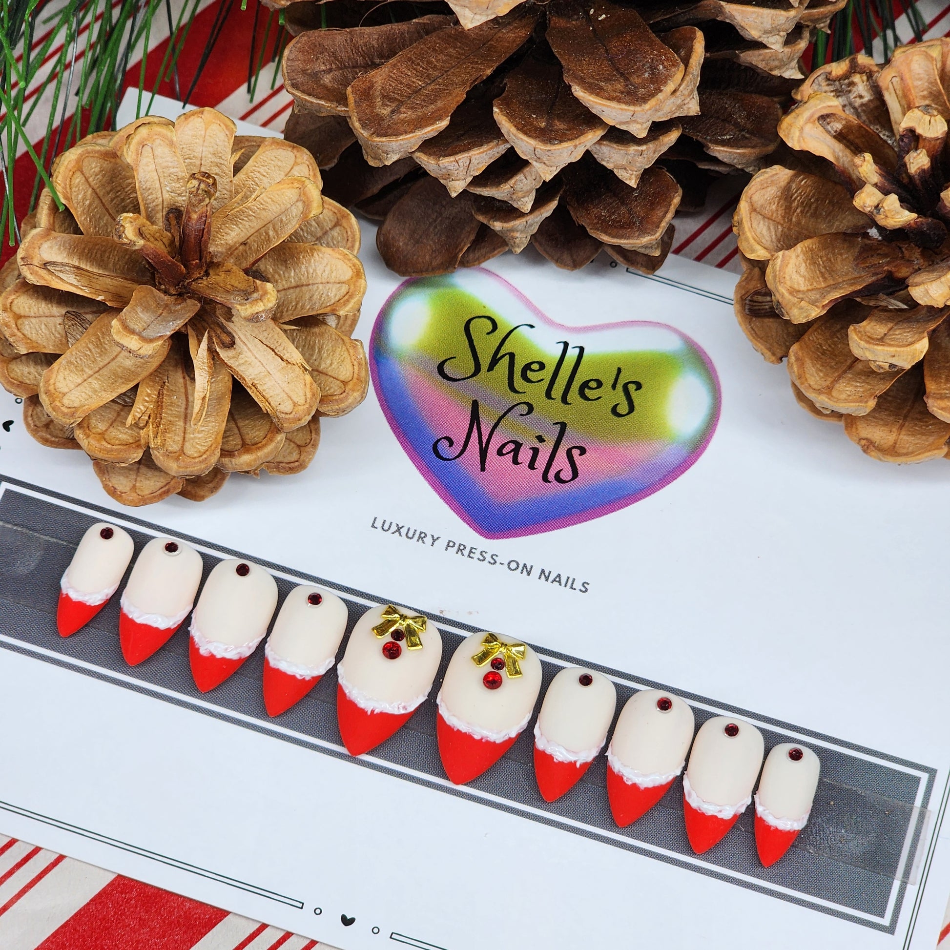 Shop our Holiday French Press-On Nails with red French tips, textured white edges, ruby gems, and gold bows. Reusable gel extensions for a festive, elegant look this season.