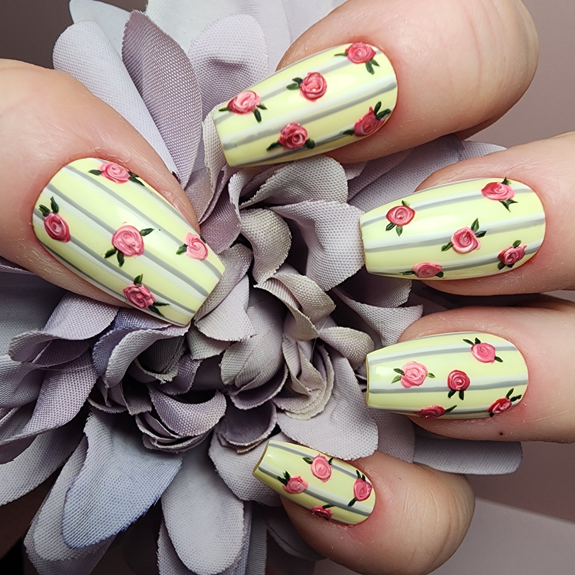 Hand-painted press-on nails with creamy pastel base, vertical grey and white stripes, and pink rosebud floral design.